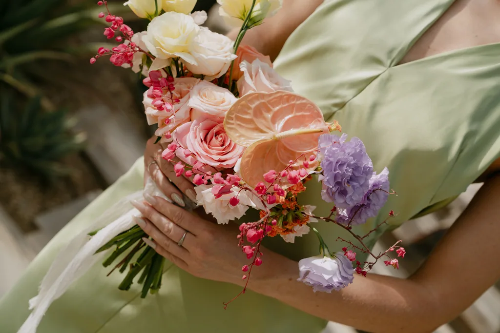 A bridesmaid's bouquet of anthurium, lilac and coral resting on sage silk