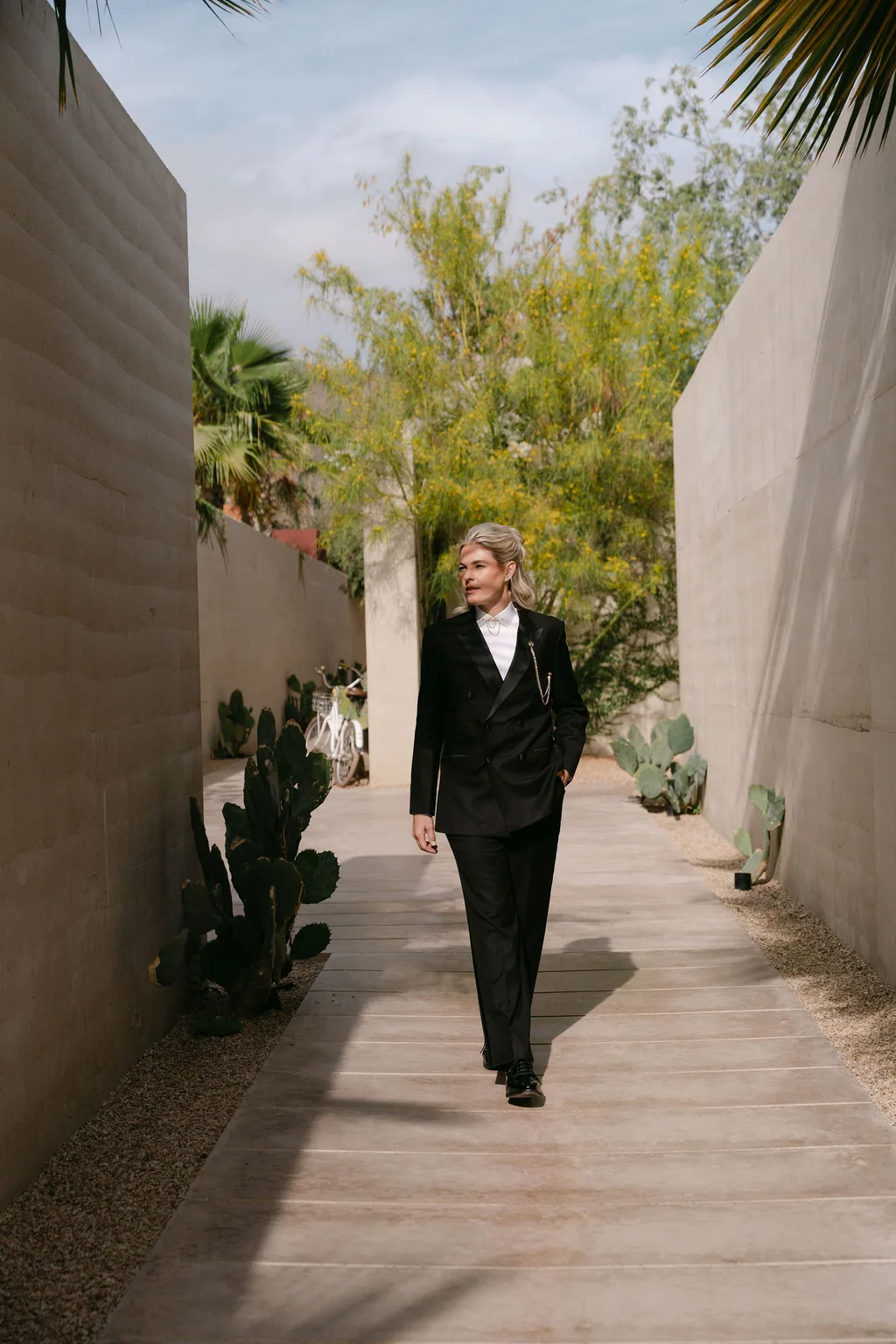 The bride in the tuxedo walking the concrete corridor between the cactus