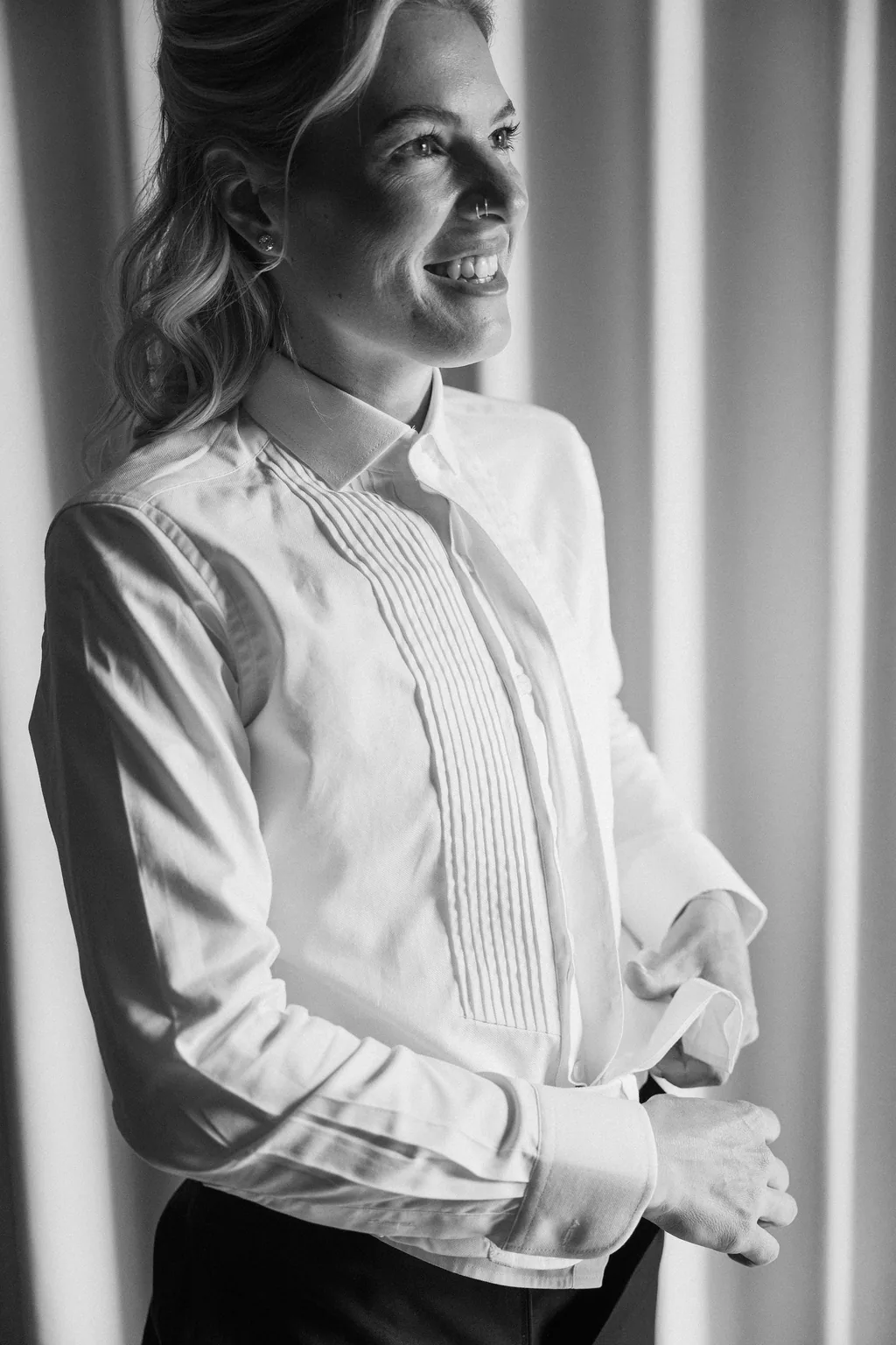The bride in the tuxedo laughing in her shirt sleeves, in black and white