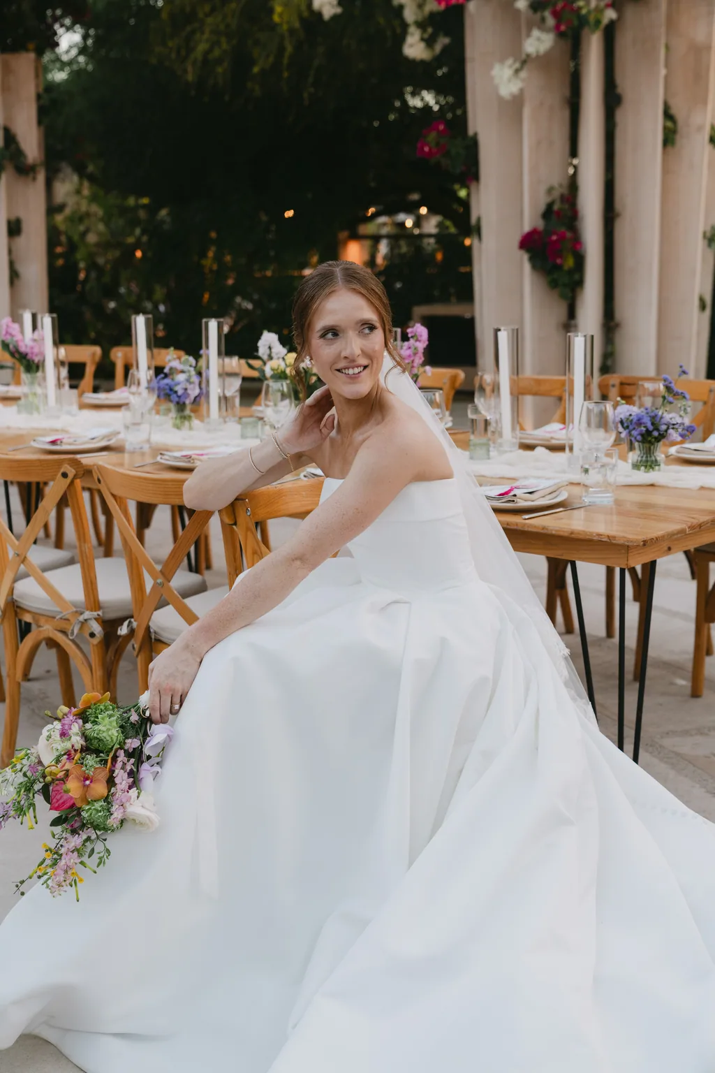 Lauren sitting at the reception table with her bouquet and her dress spread around her