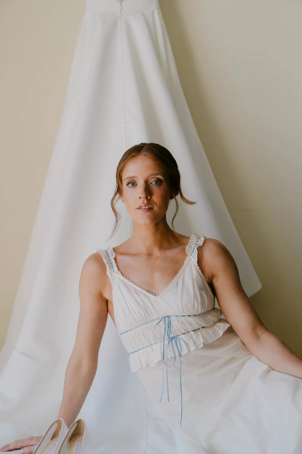 Lauren in a white slip dress, sitting in front of her hanging wedding gown