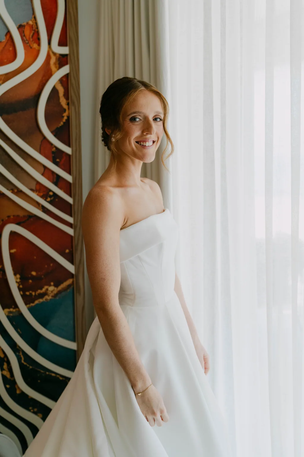 Lauren against the painted mural in the room, with the light coming through the curtain