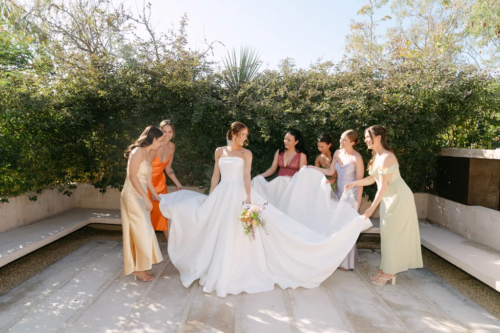 The bridesmaids standing around Lauren, holding her dress out